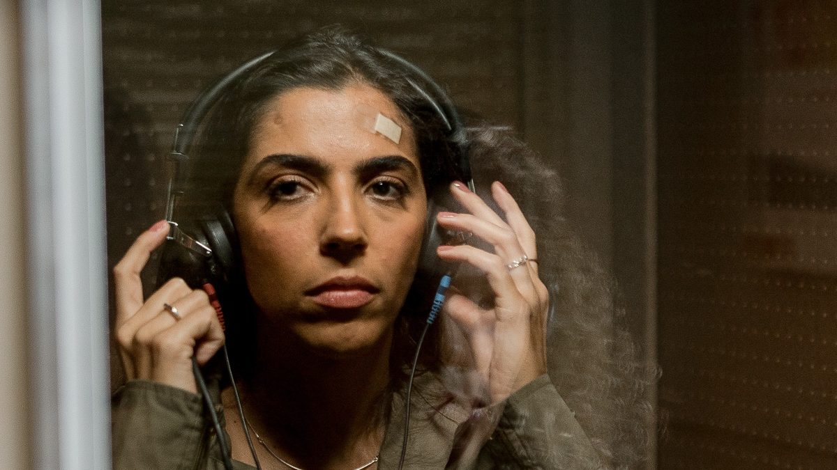 Benedita Casé Zerbini como Ana, de fones de ouvido, dentro de uma cabine de audiometria em cena de 90 Decibéis