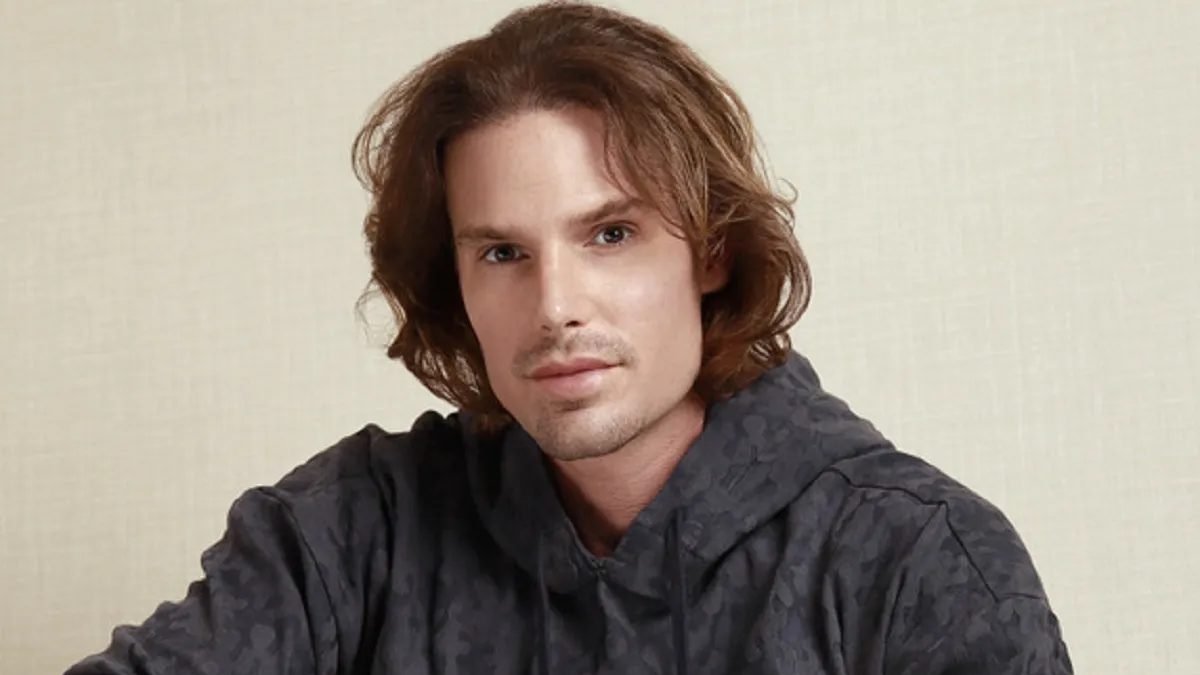 O ator Jonatas Faro, hoje participante de A Fazenda 18, de moletom cinza e cabelo na altura do ombro, em ensaio fotográfico de 2023