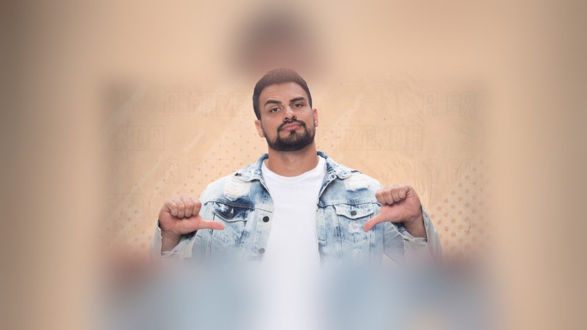 Renê Thristan, peão de A Fazenda 18, de jaqueta jeans clara e camiseta branca, faz sinal de polegar para baixo com as duas mãos