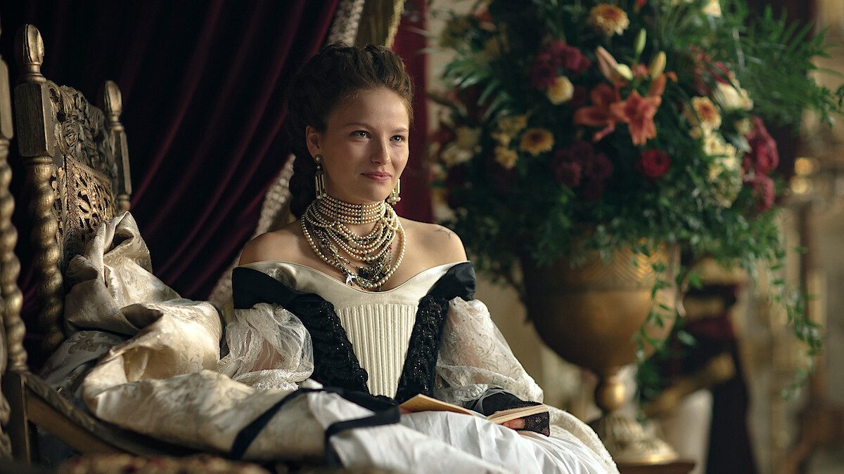 Mulher de vestido branco e preto e colar de pérolas sentada em um trono, em imagem de divulgação da 3ª temporada de A Imperatriz