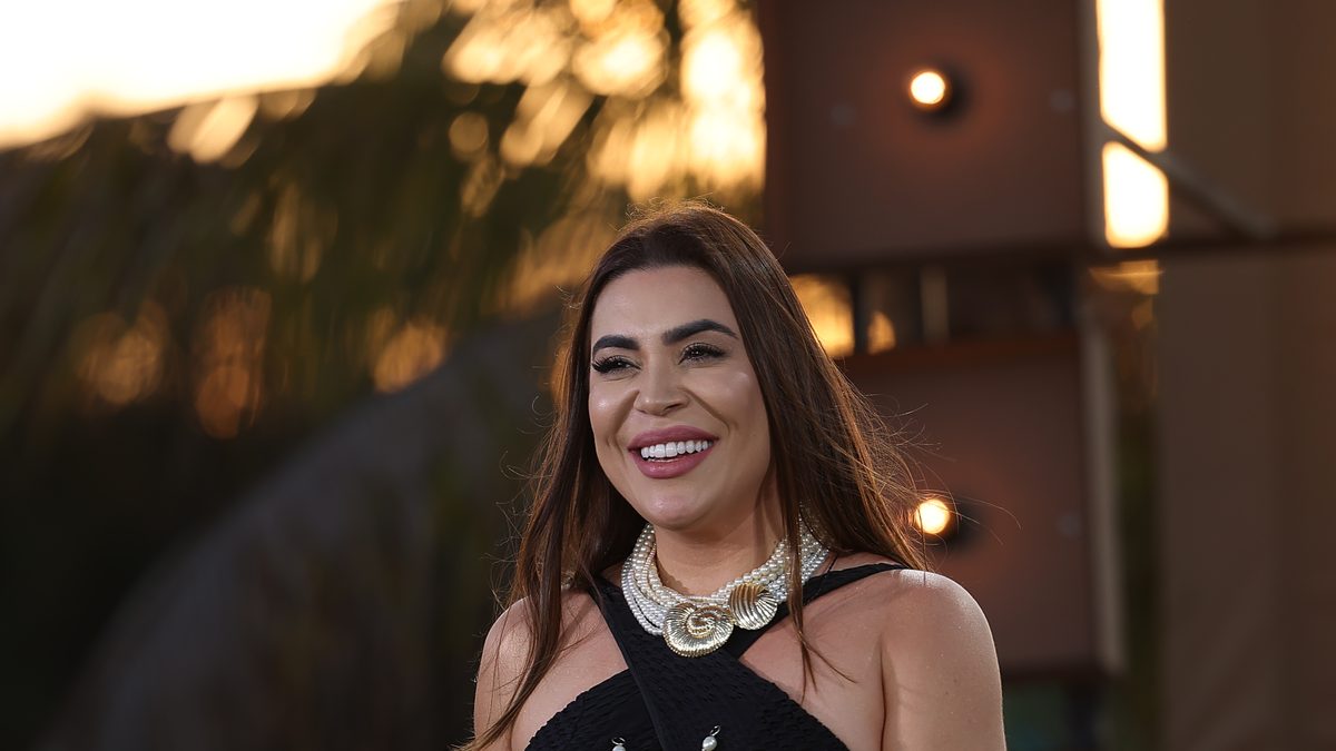 A cantora Naiara Azevedo sorri segurando o microfone durante gravação do DVD Araguaia, em 2024, com o pôr do sol ao fundo