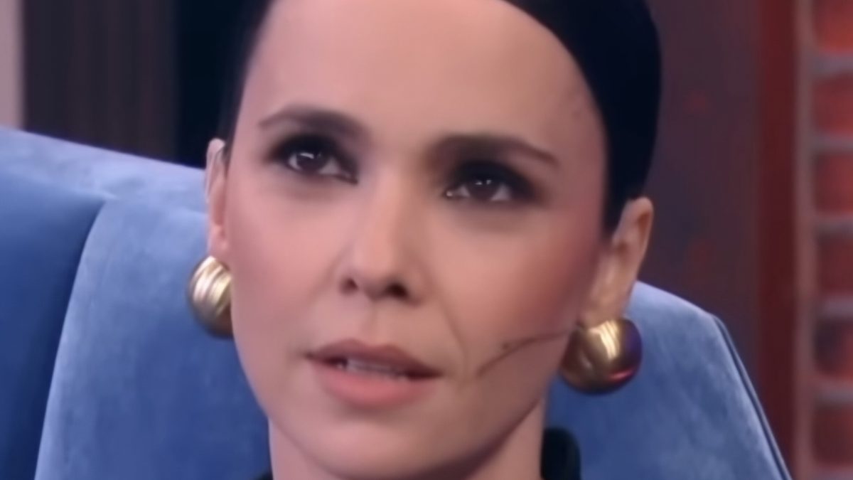 Débora Falabella em close, cabelo preso, brincos dourados, olhando para a câmera em estúdio
