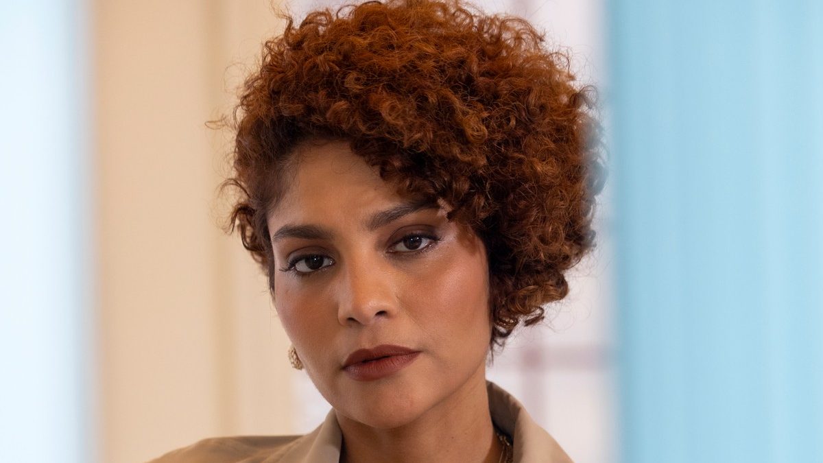 Barbara Reis, de cabelo curto cacheado e sobretudo bege, como a personagem Lúcia em Eu Não Era Louca, Era Casada