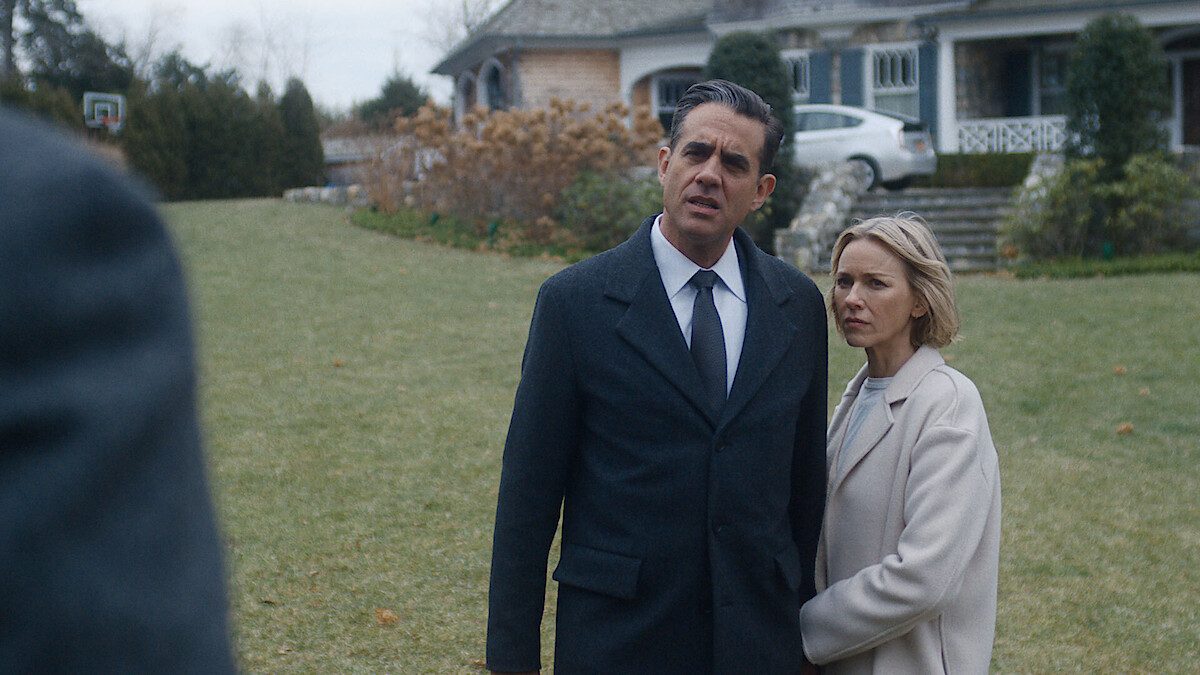 Bobby Cannavale e Naomi Watts, com expressão de espanto, diante de uma casa em cena de Bem-Vindos à Vizinhança