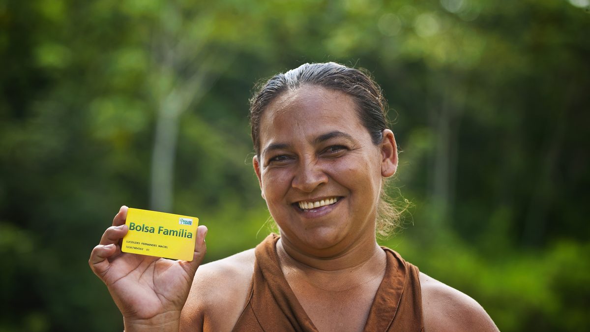Beneficiária do Bolsa Família sorri e mostra o cartão amarelo do programa, em foto de arquivo do MDS