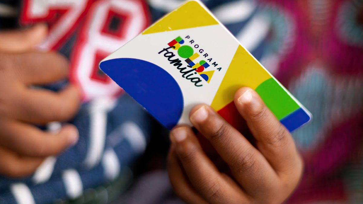 Mãos de uma criança segurando o cartão do Programa Bolsa Família, com a logomarca do programa em destaque