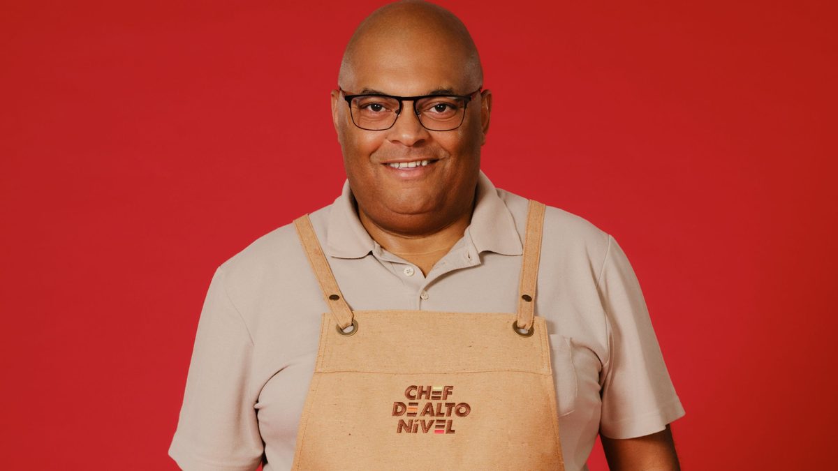 Kiko Silva, cozinheiro amador do Chef de Alto Nível 2026, de óculos e avental do programa diante de fundo vermelho