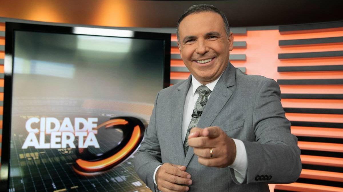 Reinaldo Gottino sorri e aponta para a câmera no cenário do Cidade Alerta, na Record