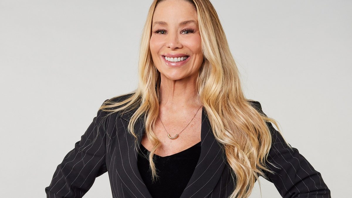 Danielle Winits sorri em retrato de estúdio, de blazer preto de risca de giz