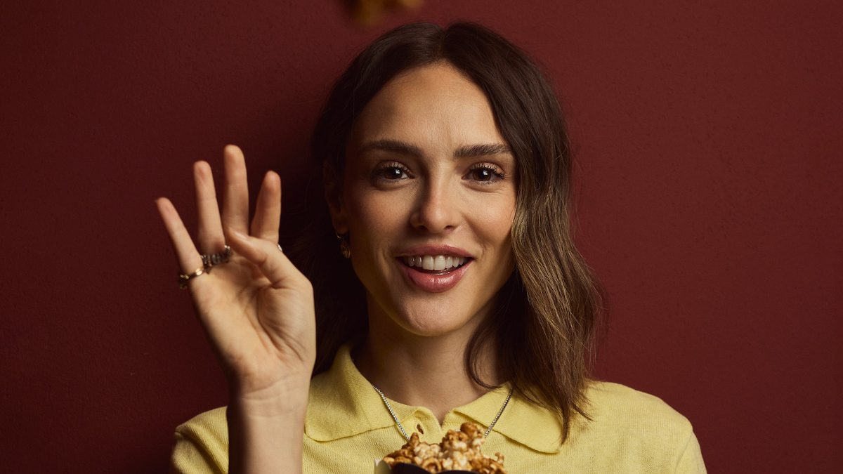 Isabelle Drummond sorri e acena, de suéter amarelo, em foto de divulgação da Netflix sobre a série Deixa Nevar