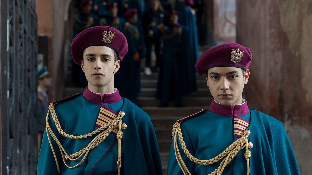 Dois cadetes de uniforme e boina olham para a câmera em cena de Escola Minerva