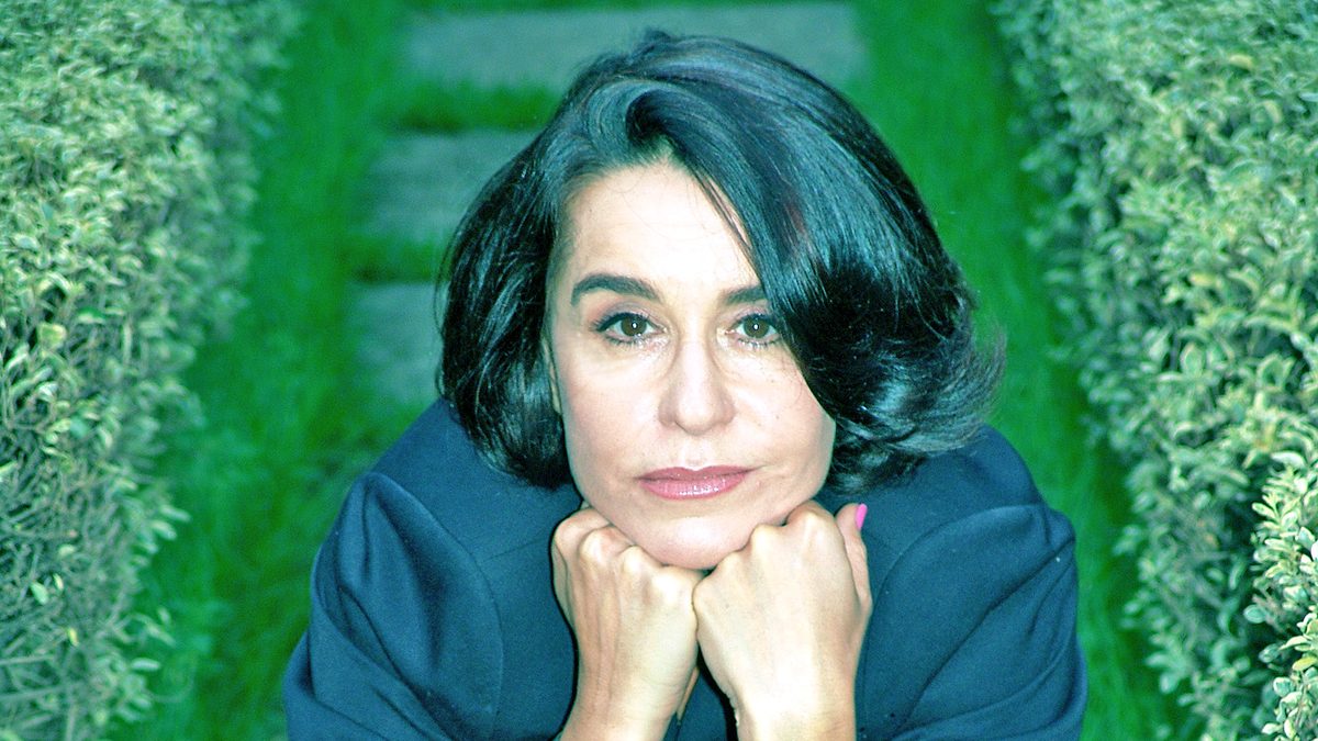 A atriz Lucélia Santos, de blazer azul-escuro, agachada num jardim com o queixo apoiado nas mãos, em foto de 2006