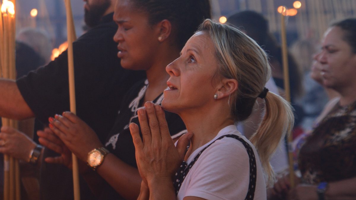 Devota reza de mãos juntas, olhando para o alto, entre outros fiéis com velas no Santuário Nacional de Aparecida, no Dia da Padroeira, em 12 de outubro de 2017