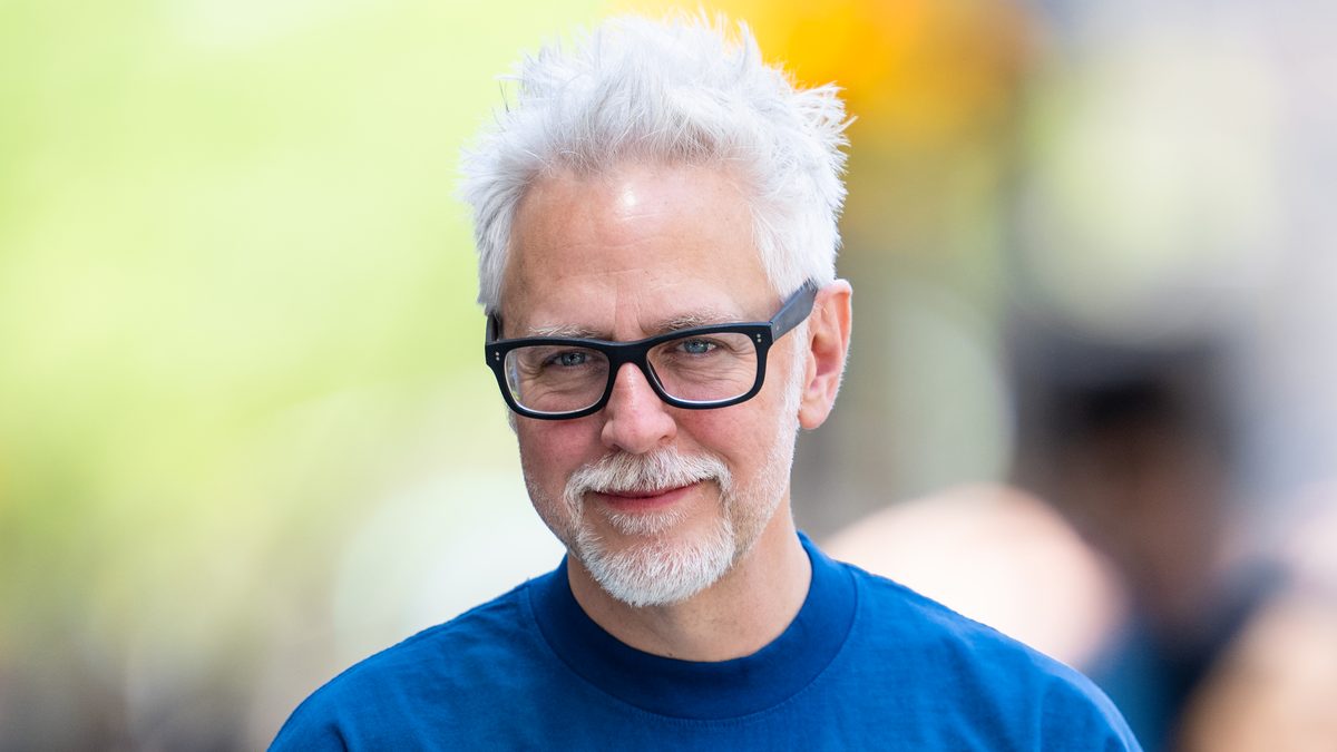 James Gunn, de óculos e camiseta azul, sorri para a câmera em foto de junho de 2024
