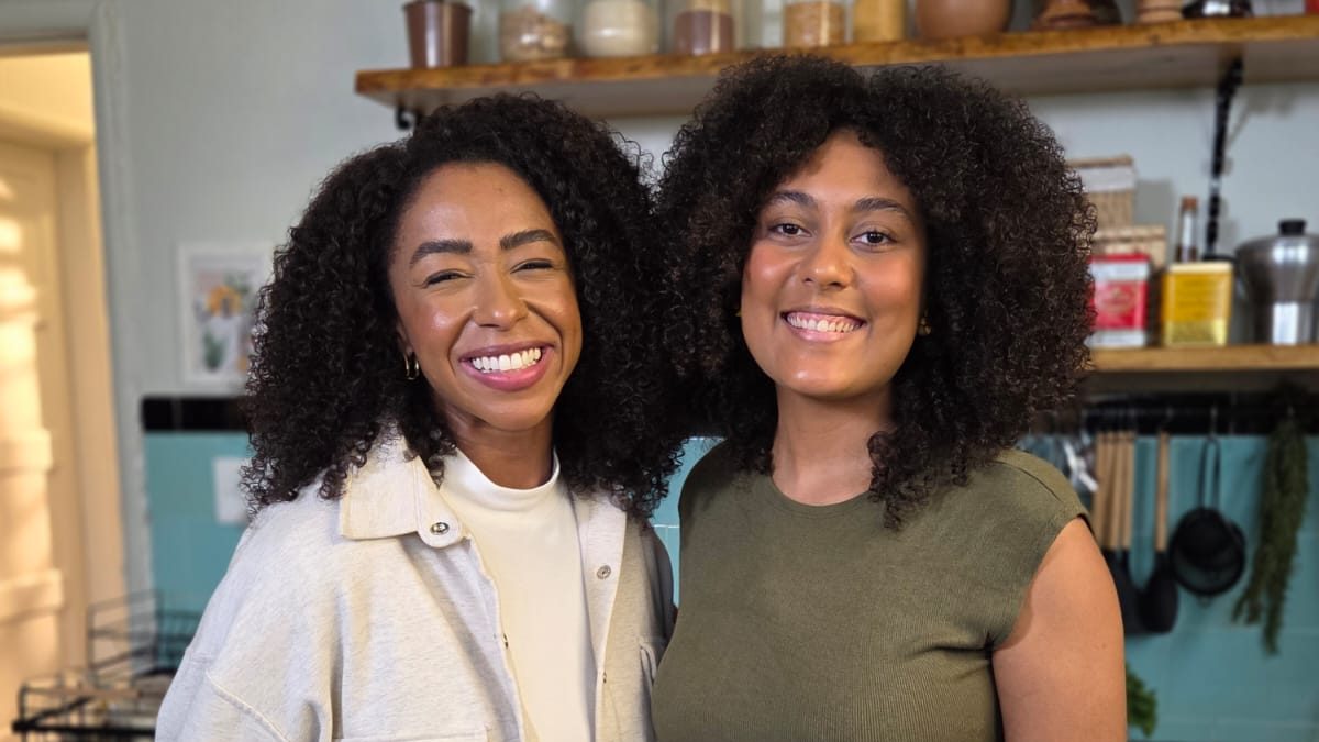 A repórter Mariana Bispo e a cozinheira Thallita Flor sorriem lado a lado em uma cozinha, nas gravações do Globo Repórter sobre proteínas