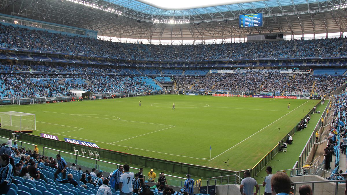 Interior da Arena do Grêmio, em Porto Alegre, com torcedores nas arquibancadas azuis e o gramado ao centro (foto de arquivo de 2014)