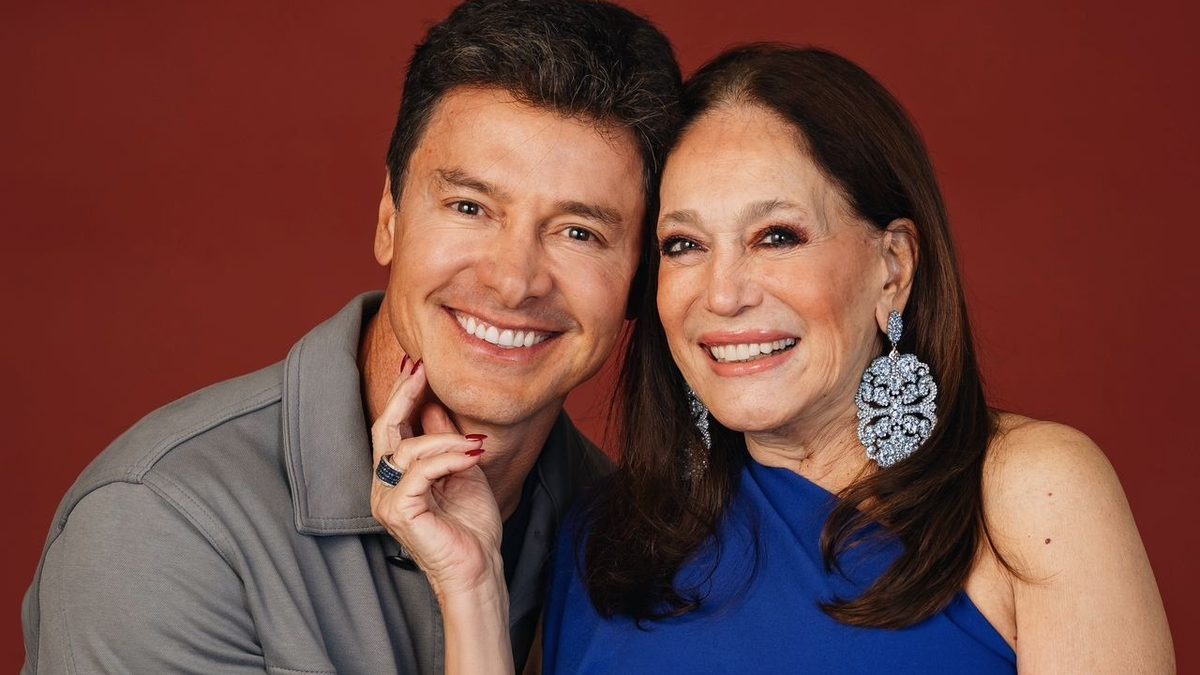 Rodrigo Faro e Susana Vieira sorriem abraçados diante de um fundo vermelho, em foto de divulgação do reality Herança em Jogo, do Globoplay