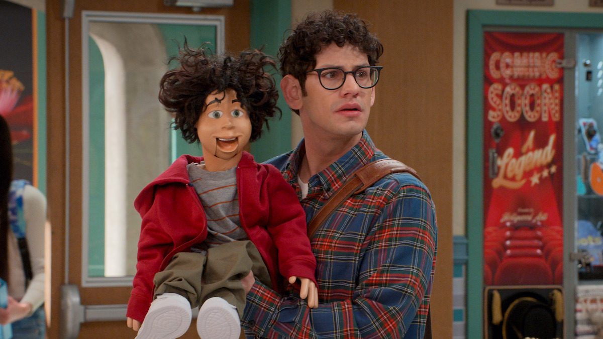 Matt Bennett como Robbie Shapiro, segurando um boneco de ventríloquo, nos corredores da escola em Hollywood Arts, série derivada de Brilhante Victória na Netflix