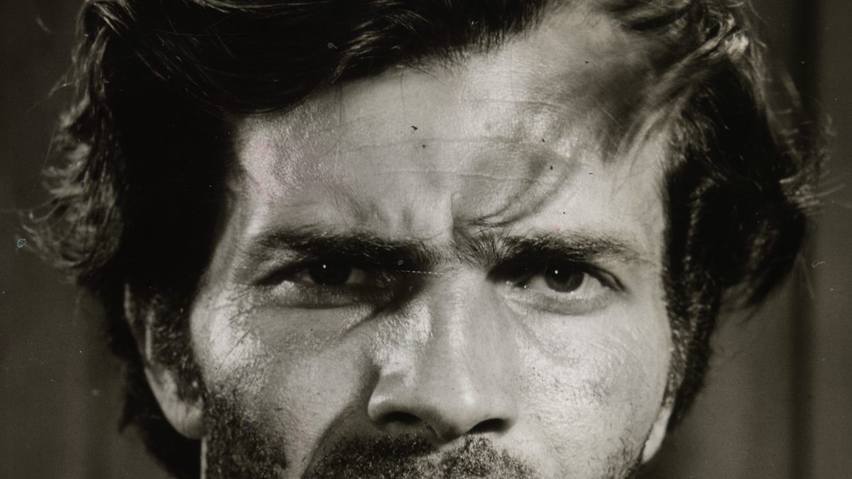 Retrato em preto e branco de Tarcísio Meira jovem, de barba por fazer e cenho franzido