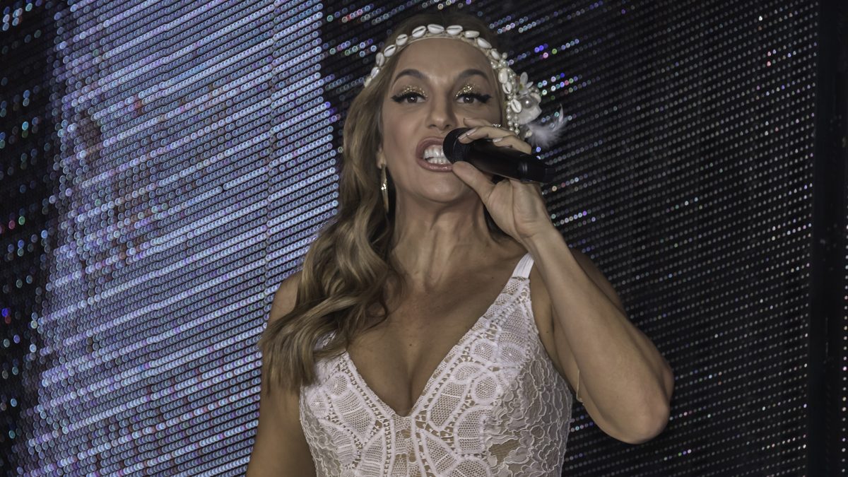 A cantora Ivete Sangalo canta ao microfone num show em 2016, de vestido branco rendado e tiara de conchas
