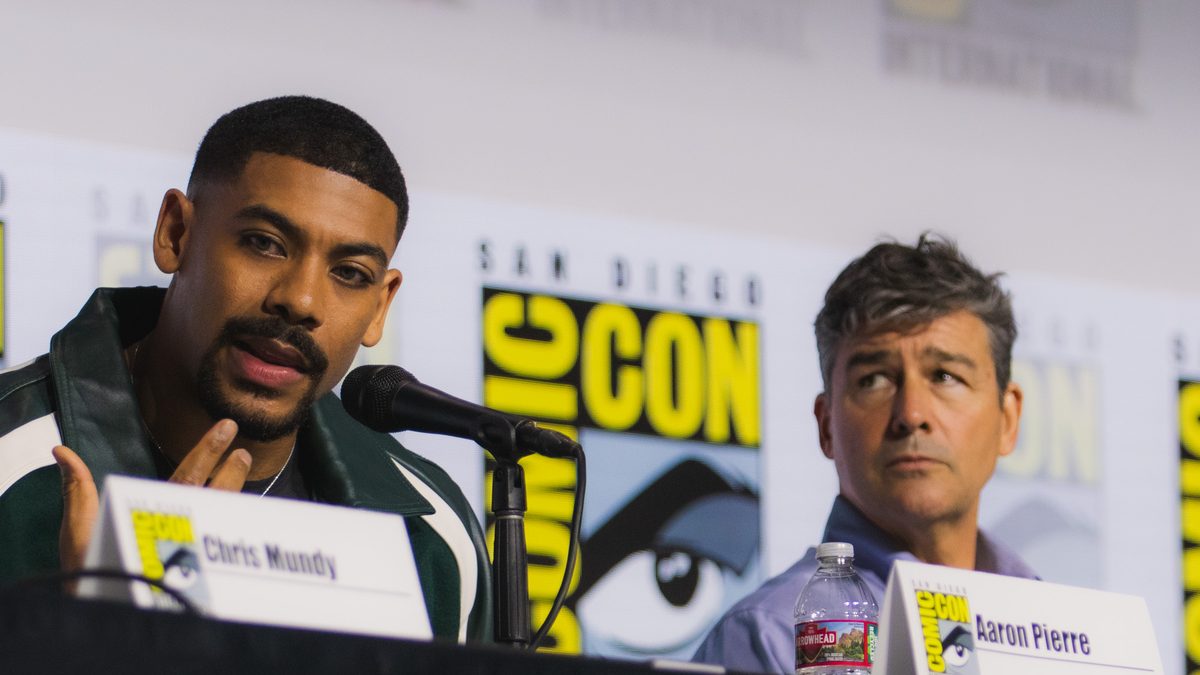 Aaron Pierre, de jaqueta verde, fala ao microfone no painel de Lanternas na San Diego Comic-Con de 2026, com Kyle Chandler ao lado