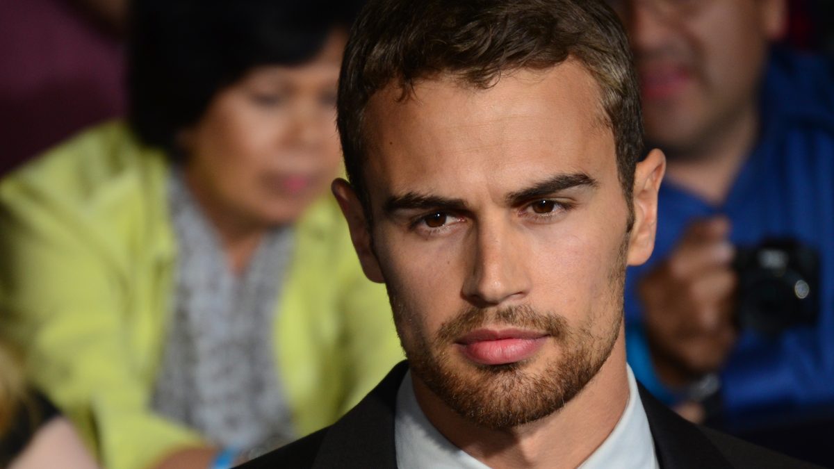 O ator Theo James, de terno preto e barba por fazer, num evento em março de 2014