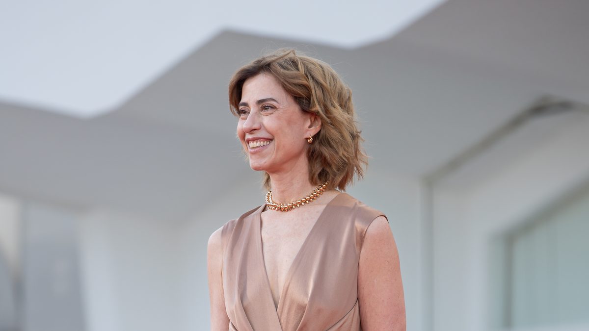 A atriz Fernanda Torres, de vestido cor de bronze e colar dourado, sorri na passarela do Festival de Veneza, em 2025