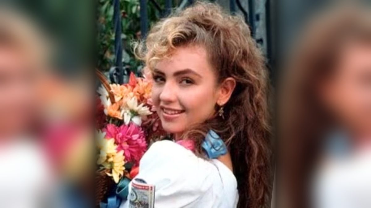 Thalía como Maria Mercedes, sorrindo com um cesto de flores e bilhetes de loteria, em foto de divulgação da novela
