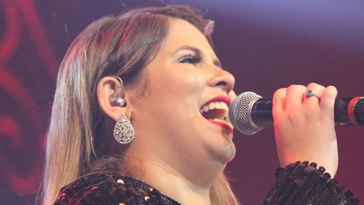Marília Mendonça canta ao microfone, de vestido de paetês preto, em show de 2017
