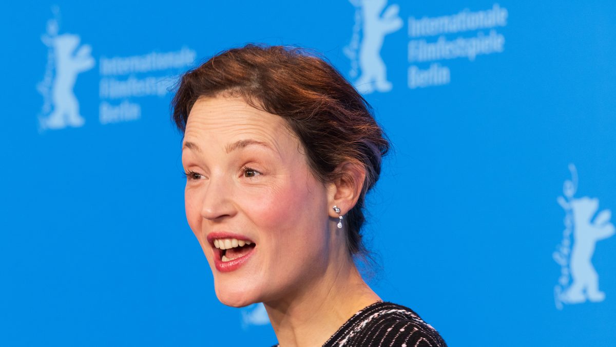 A atriz Vicky Krieps, que vive a empregada Maggie em Monstro: A História de Lizzie Borden, fala sorrindo diante do painel azul do Festival de Berlim