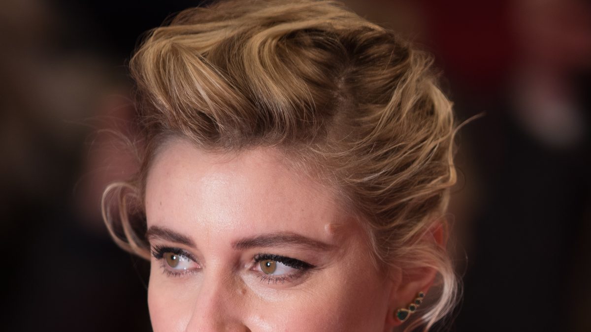Greta Gerwig, de cabelo loiro preso, olhando para o lado na Berlinale de 2018