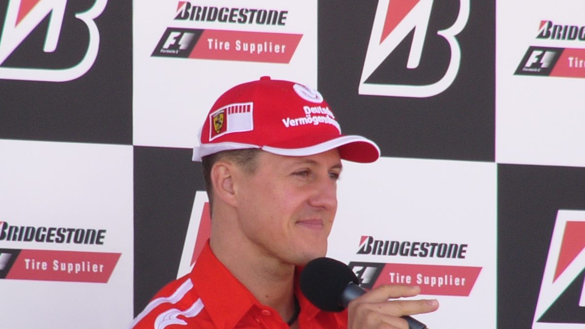 Michael Schumacher, tema do documentário Schumacher 94 da Netflix, de boné e camisa vermelhos da Ferrari, fala ao microfone em entrevista no GP dos Estados Unidos de 2005