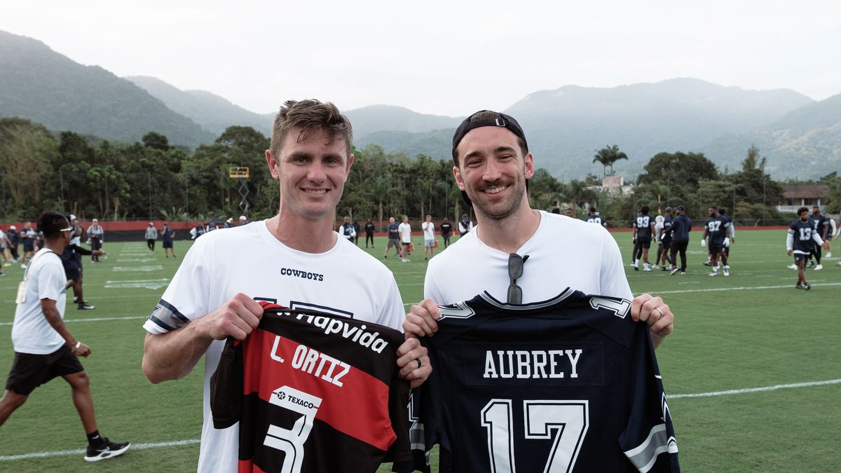 Léo Ortiz, do Flamengo, e um jogador do Dallas Cowboys no Ninho do Urubu, cada um segurando a camisa do outro time, com os nomes Ortiz e Aubrey