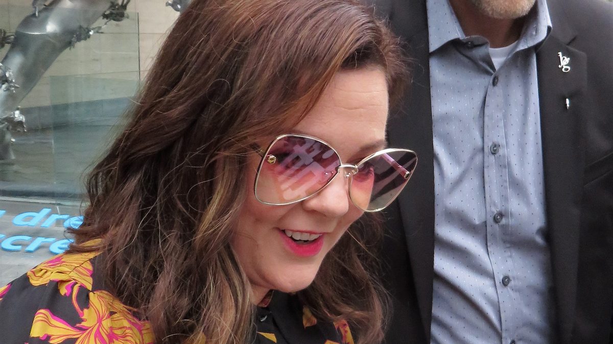 A atriz Melissa McCarthy, de óculos escuros e blusa florida, sorri no Festival de Toronto de 2018