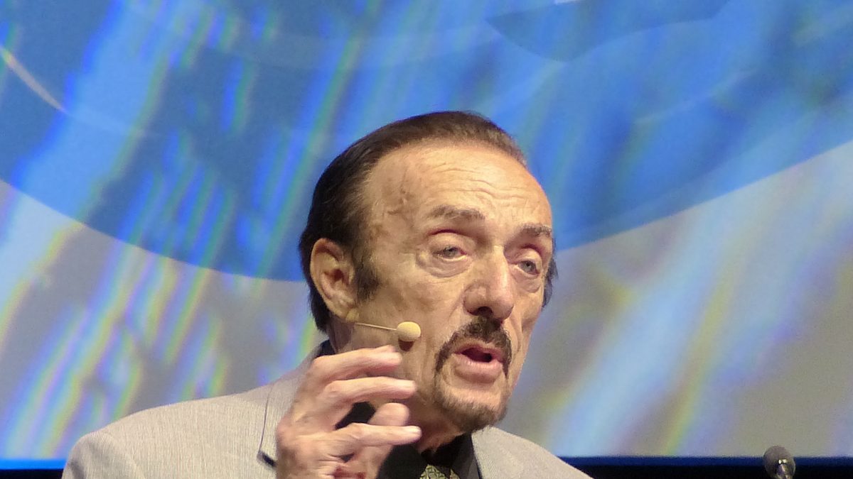 O psicólogo Philip Zimbardo, autor do experimento de Stanford de 1971, fala com microfone de lapela e gesticula durante conferência em Budapeste, em 2017