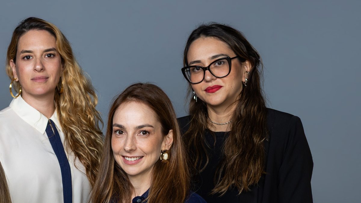 Três integrantes da equipe feminina da série O Testamento: O Segredo de Anita Harley posam em estúdio de fundo cinza, em foto de divulgação da Globo