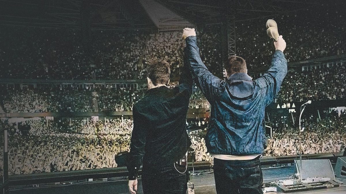 Dois homens de costas, de braços erguidos diante de um estádio lotado, em imagem do documentário sobre a turnê do Oasis