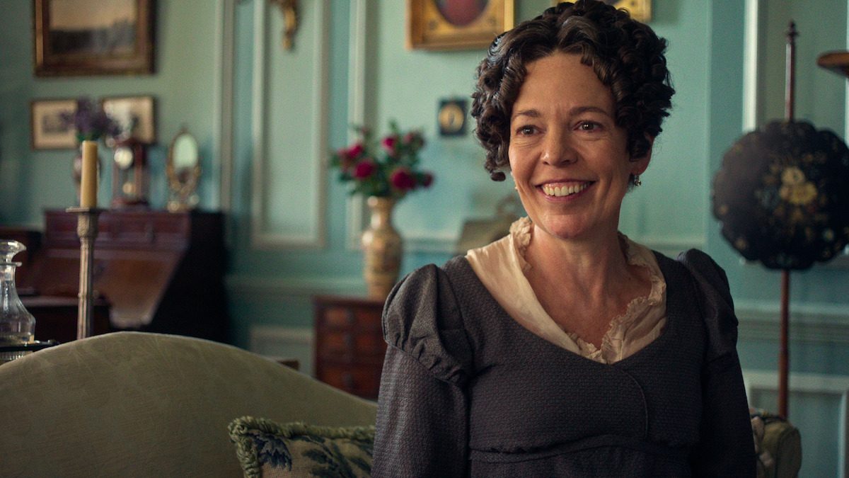 Olivia Colman, como a Senhora Bennet, sorri sentada num sofá de uma sala de estar verde, em foto de divulgação da série Orgulho e Preconceito