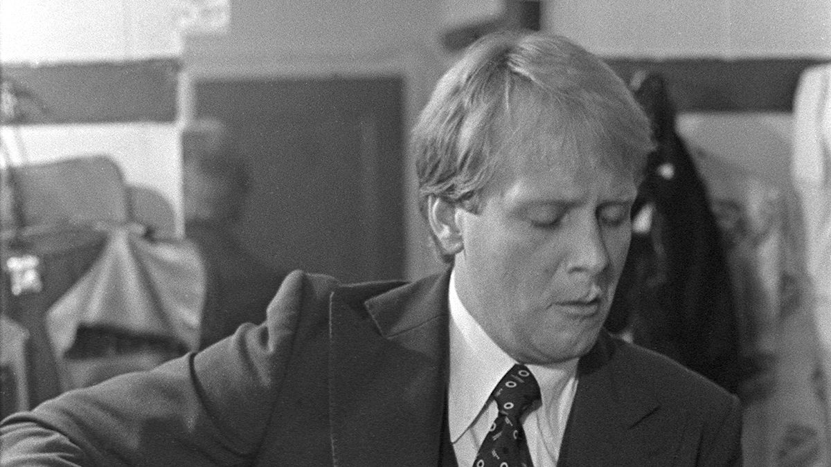 Martin Mull tocando guitarra elétrica de caixa, de terno e gravata, em foto em preto e branco de maio de 1976