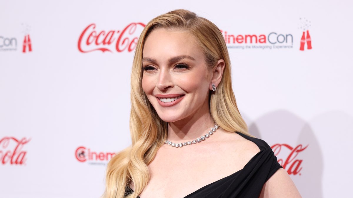 A atriz Lindsay Lohan, de cabelo loiro e vestido preto, sorri no tapete vermelho da CinemaCon 2025, em Las Vegas