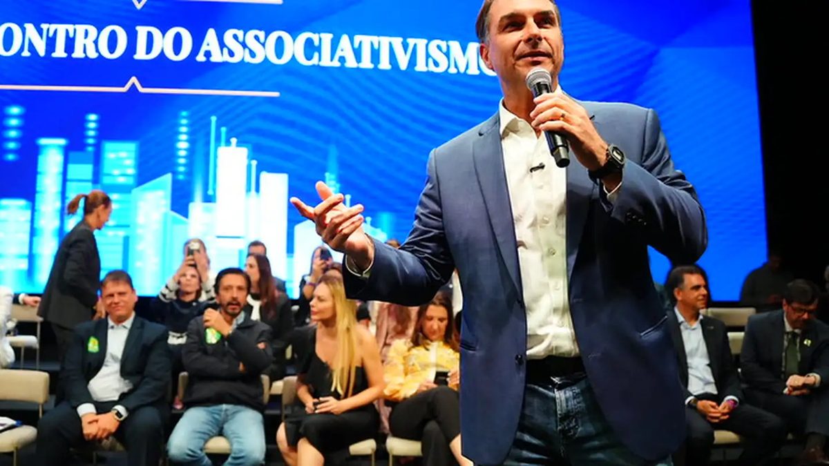 O candidato Flávio Bolsonaro, de blazer azul, fala ao microfone em palco do Grande Encontro do Associativismo, em São Paulo, em 13 de outubro de 2026