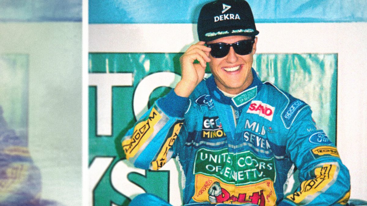 Michael Schumacher sorrindo, de boné e óculos escuros, com o macacão azul da Benetton de 1994, na imagem de divulgação do documentário Schumacher 94 da Netflix