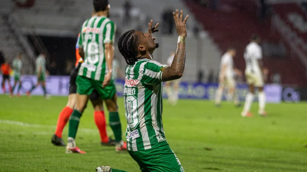 Jogador do Juventude, de camisa listrada verde e branca, ajoelhado no gramado molhado com as mãos para o alto, em jogo da Série B