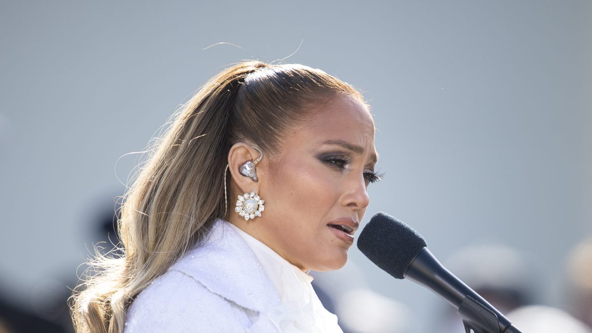Jennifer Lopez, de casaco branco e rabo de cavalo, canta ao microfone no Capitólio dos Estados Unidos, em Washington, em janeiro de 2021