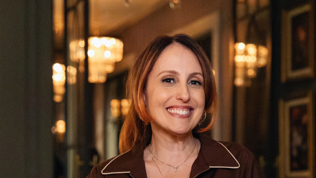 Luana Martau caracterizada como Tilde, de uniforme marrom e avental branco, sorrindo, em foto de divulgação de Quem Ama Cuida