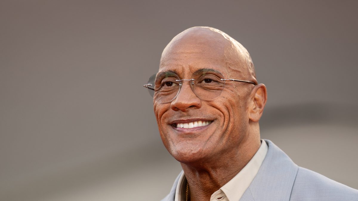 Dwayne Johnson, protagonista de Adão Negro, sorri de óculos e terno cinza claro em evento em setembro de 2025
