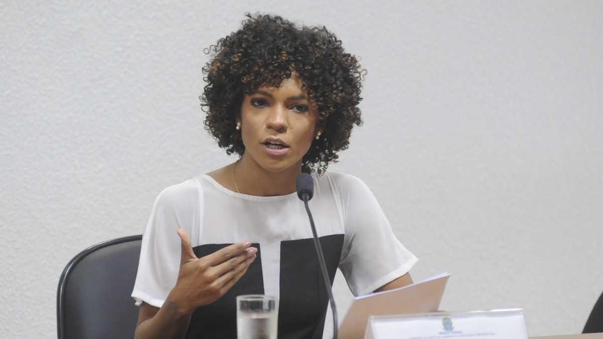 A jornalista Luciana Barreto, de cabelo cacheado e blusa branca e preta, fala em audiência pública no Senado, em 2015