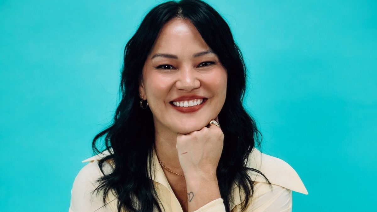 Geovanna Tominaga sorri sentada, com a mão no queixo, em foto de divulgação da Globo para a edição especial da TV Globinho