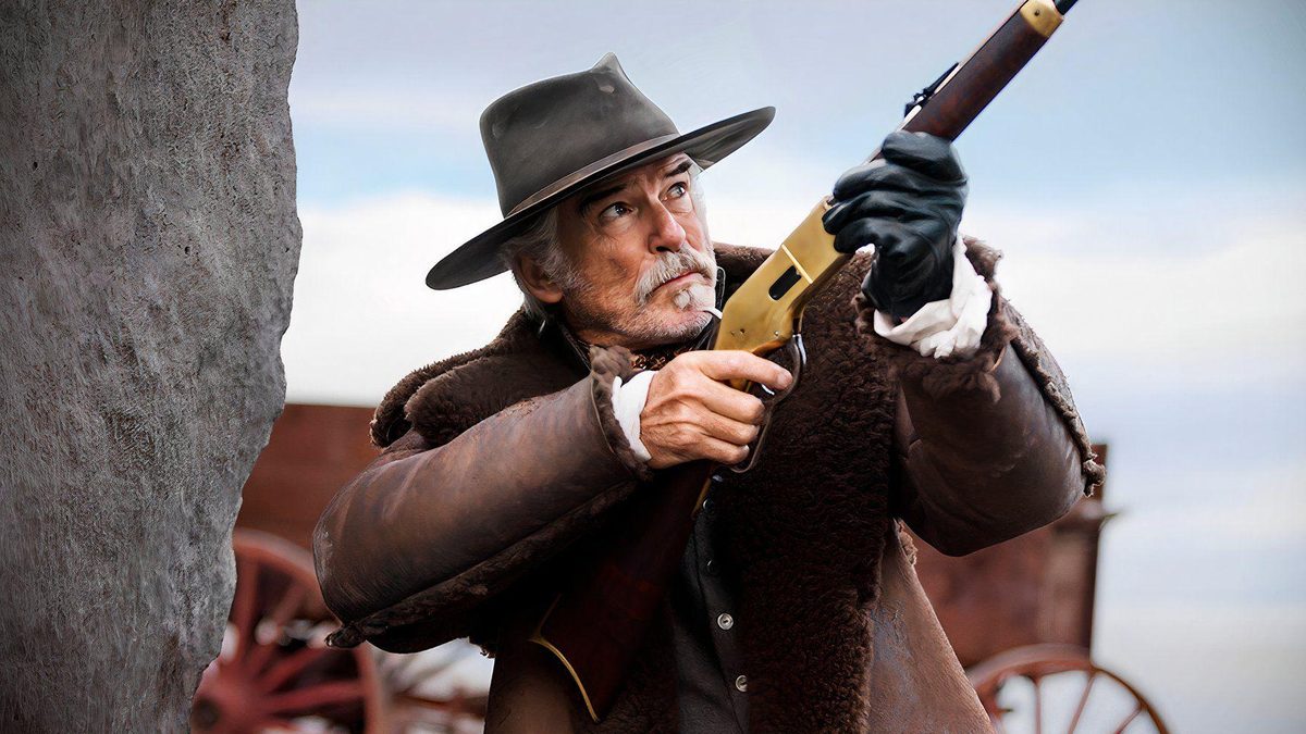 Pierce Brosnan, de chapéu e casaco de pele, aponta um rifle dourado em Vingança Brutal