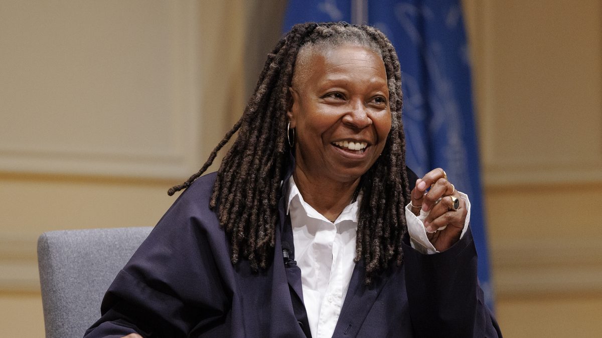 A atriz Whoopi Goldberg, de tranças e blazer escuro, sorri sentada durante um evento na Biblioteca do Congresso dos Estados Unidos, em 2024